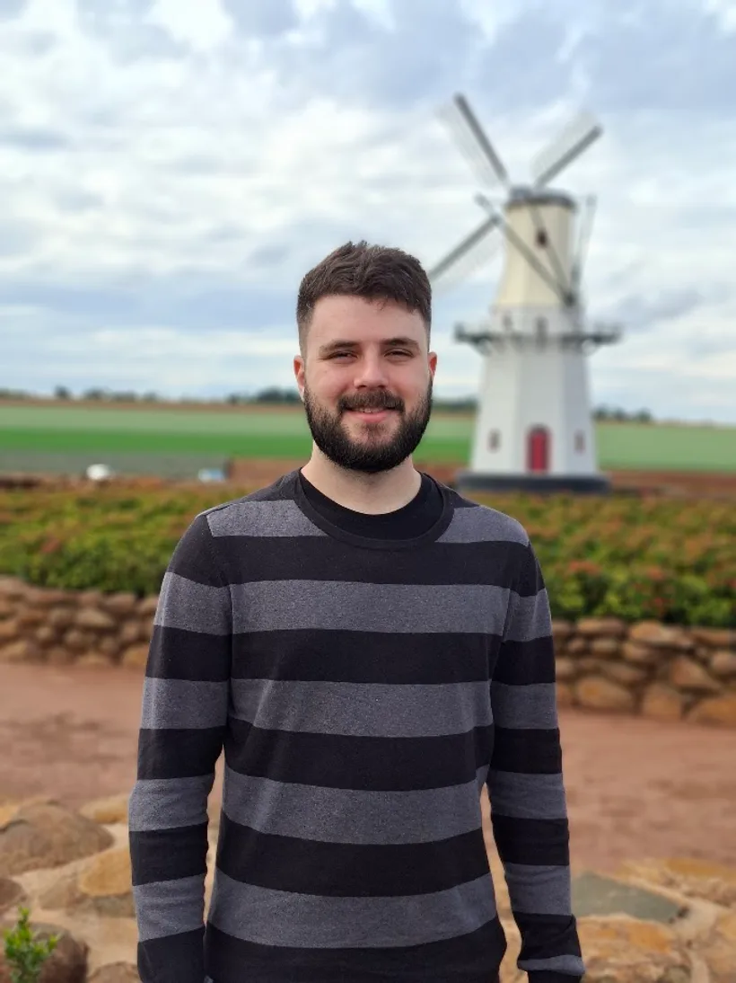 Eduardo em pé ao ar livre, com um moinho de vento ao fundo